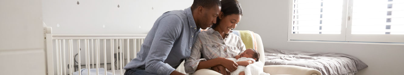 Mother and father looking down at their baby in a white room.